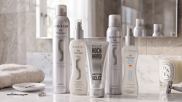 Five Biosilk styling products in silver and white, including hairsprays and Rock Hard gel&eacute;e, on a bathroom counter.